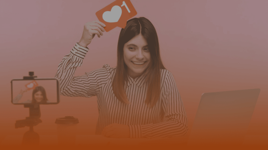 Whissel Strategies A woman sitting at a desk holds up a card with a heart and the number one, while recording herself with a smartphone and tripod. Toronto Digital Marketing Agency