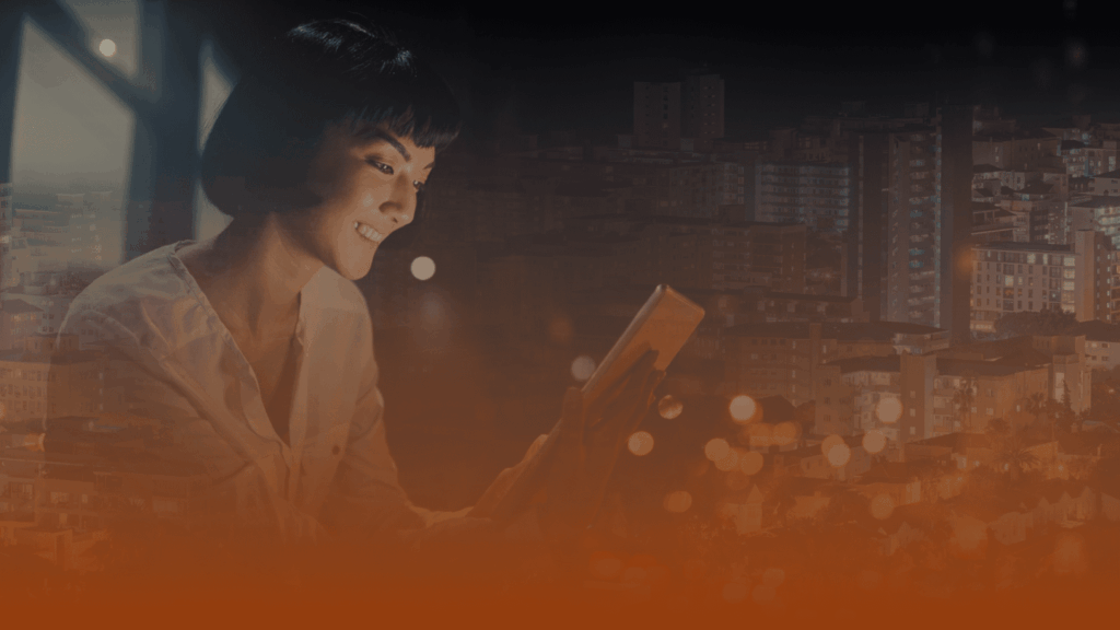 Whissel Strategies A woman sits by a window at night, smiling while using a tablet, with the blurred cityscape illuminated in the background. Toronto Digital Marketing Agency