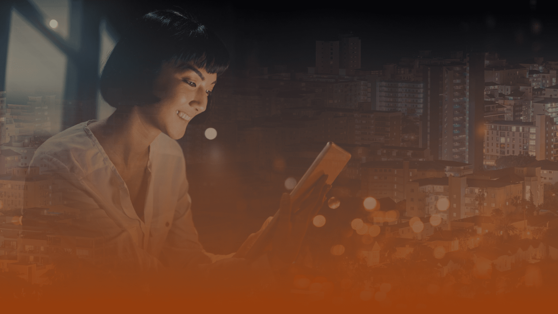 Whissel Strategies A woman sits by a window at night, smiling while using a tablet, with the blurred cityscape illuminated in the background. Toronto Digital Marketing Agency