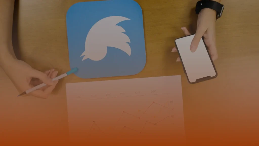 Whissel Strategies A person holds a smartphone above a desk with a bird logo on a blue square, a chart, and another hand holding a pen. Toronto Digital Marketing Agency
