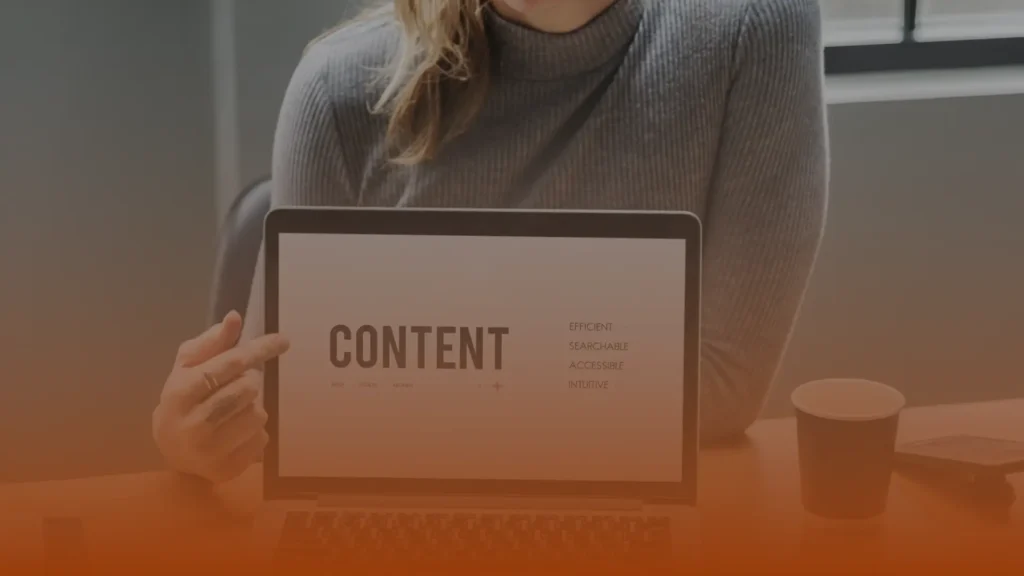 Whissel Strategies A person in a gray sweater holds a laptop displaying the word "CONTENT" and related terms on the screen, seated at a table with a coffee cup. Toronto Digital Marketing Agency