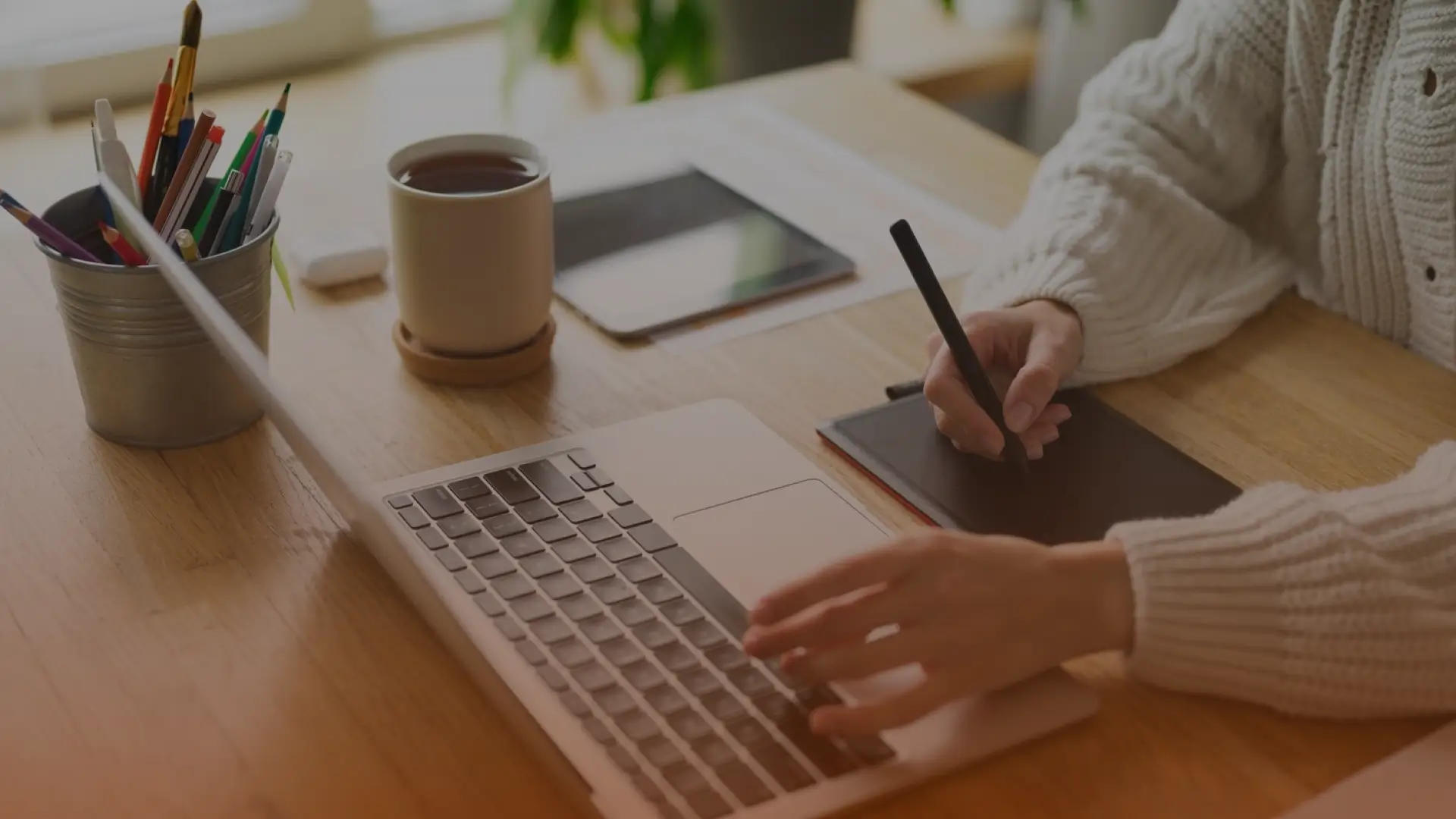 Whissel Strategies Person using a laptop and graphic tablet at a wooden desk with a cup of coffee, tablet, and pencils nearby. Toronto Digital Marketing Agency