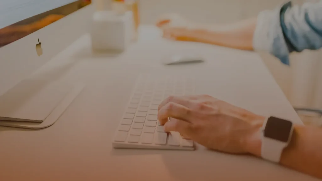 Whissel Strategies A person types on a wireless keyboard at a tidy desk with a computer, mouse, and another person’s hand visible in the background. Toronto Digital Marketing Agency