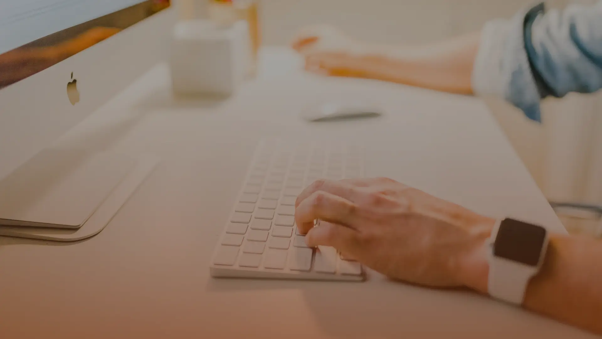Whissel Strategies A person types on a wireless keyboard at a tidy desk with a computer, mouse, and another person’s hand visible in the background. Toronto Digital Marketing Agency