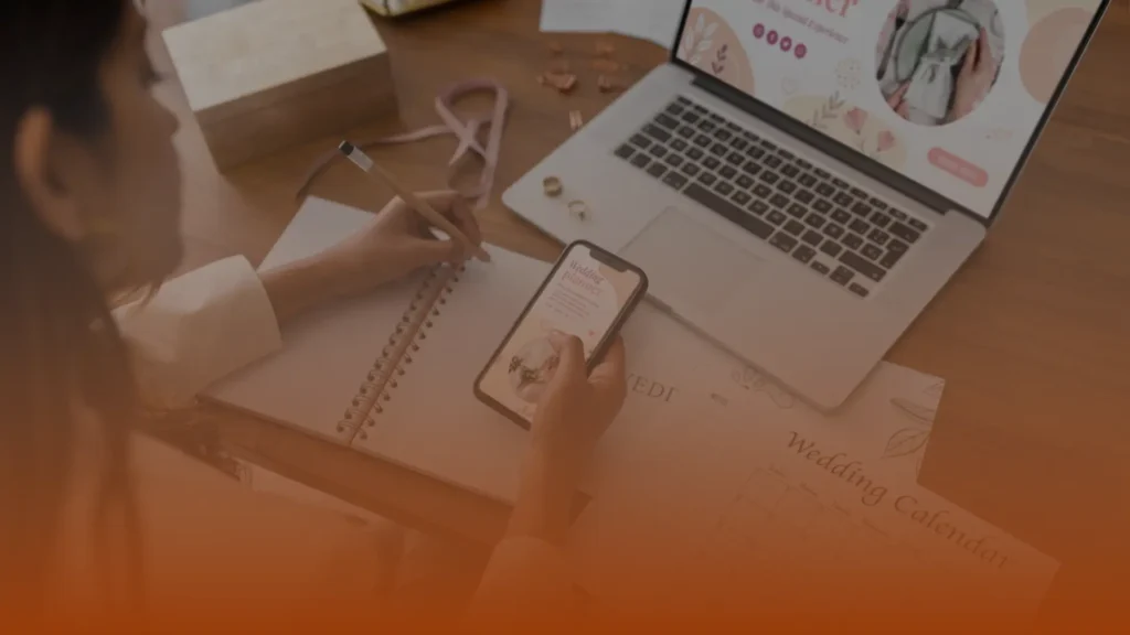 Whissel Strategies Person writing in a notebook while holding a smartphone, with an open laptop and a wedding calendar on the desk. Toronto Digital Marketing Agency