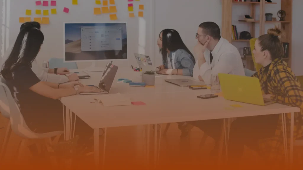 Whissel Strategies Five people sit around a table with laptops, watching a presentation on a large monitor in a modern office with sticky notes on the wall. Toronto Digital Marketing Agency
