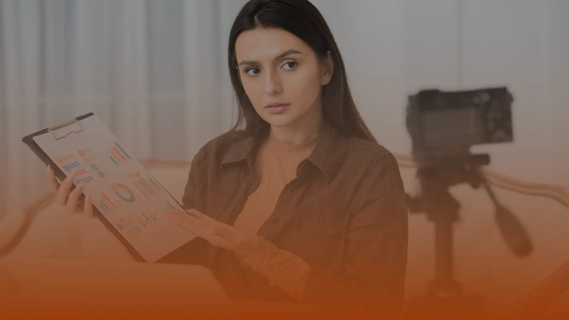Whissel Strategies A woman holds up a clipboard displaying charts and graphs, sitting indoors with a camera on a tripod in the background. Toronto Digital Marketing Agency