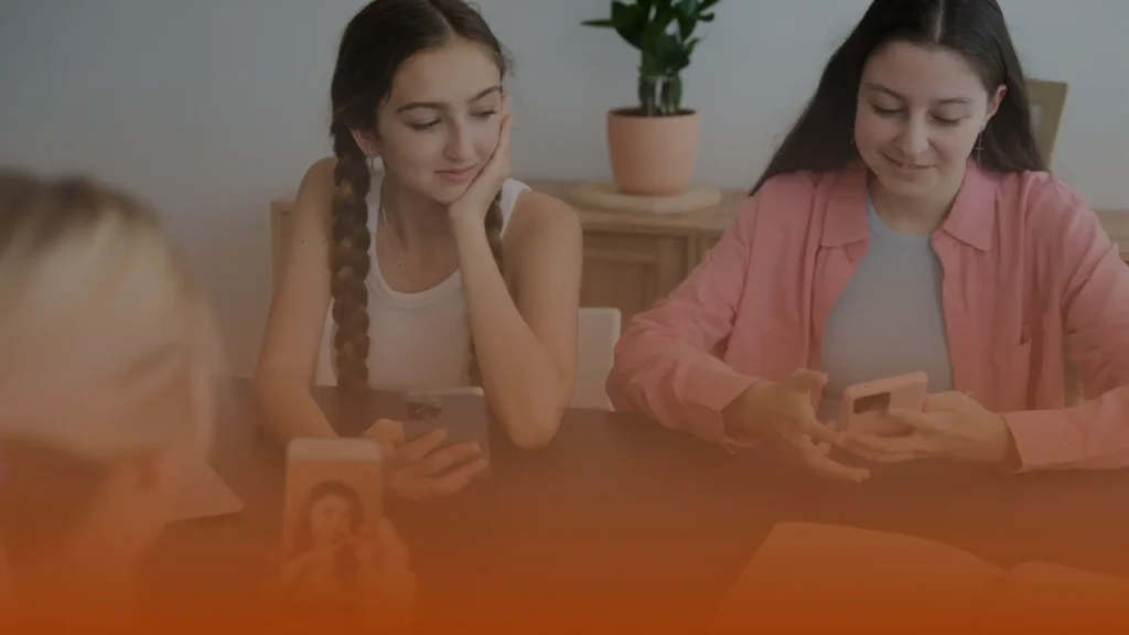 Whissel Strategies Two young women sit at a table using their smartphones, with a potted plant and books visible in the background. Toronto Digital Marketing Agency