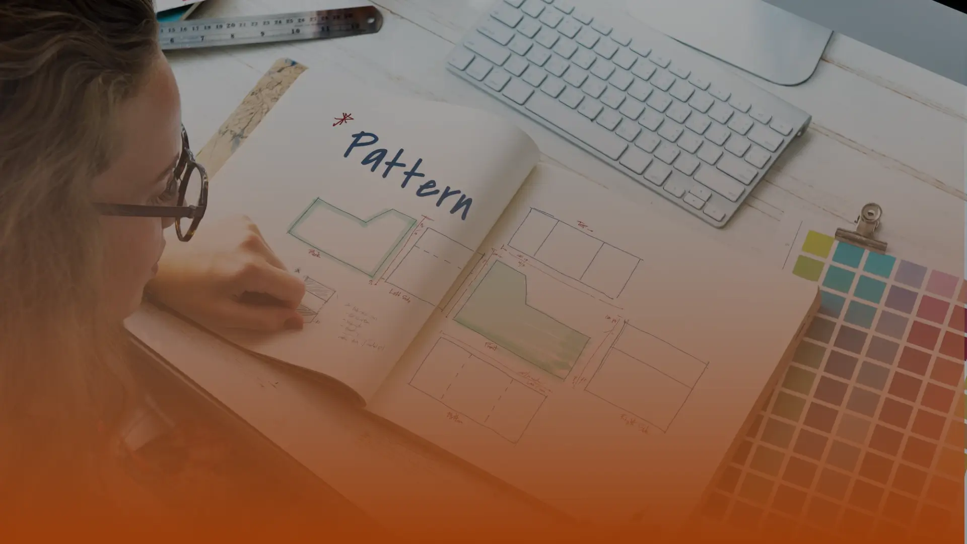 Whissel Strategies A person reviews a pattern design sketchbook with technical drawings, sitting at a desk with a keyboard, color swatches, and ruler. Toronto Digital Marketing Agency