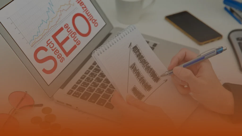 Whissel Strategies Person drawing a bar graph in a notebook beside a laptop displaying an SEO (Search Engine Optimization) chart. Toronto Digital Marketing Agency