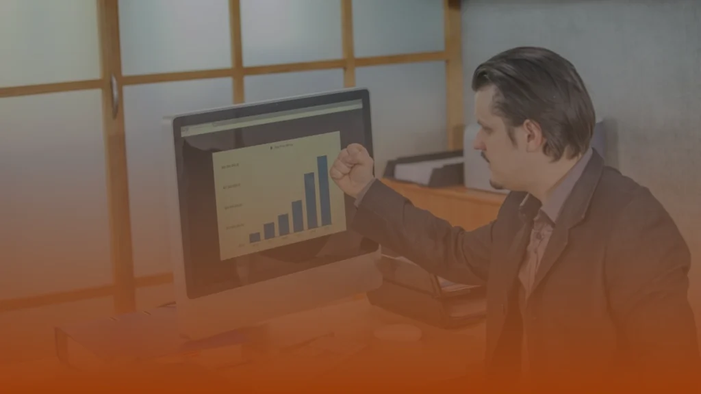 Whissel Strategies A man in a suit sits at a desk, making a fist gesture while looking at a computer screen displaying an upward-trending bar graph. Toronto Digital Marketing Agency