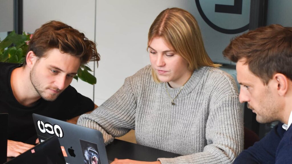 Whissel Strategies Three people are sitting at a table, looking at laptops and discussing something in an office setting. Toronto Digital Marketing Agency