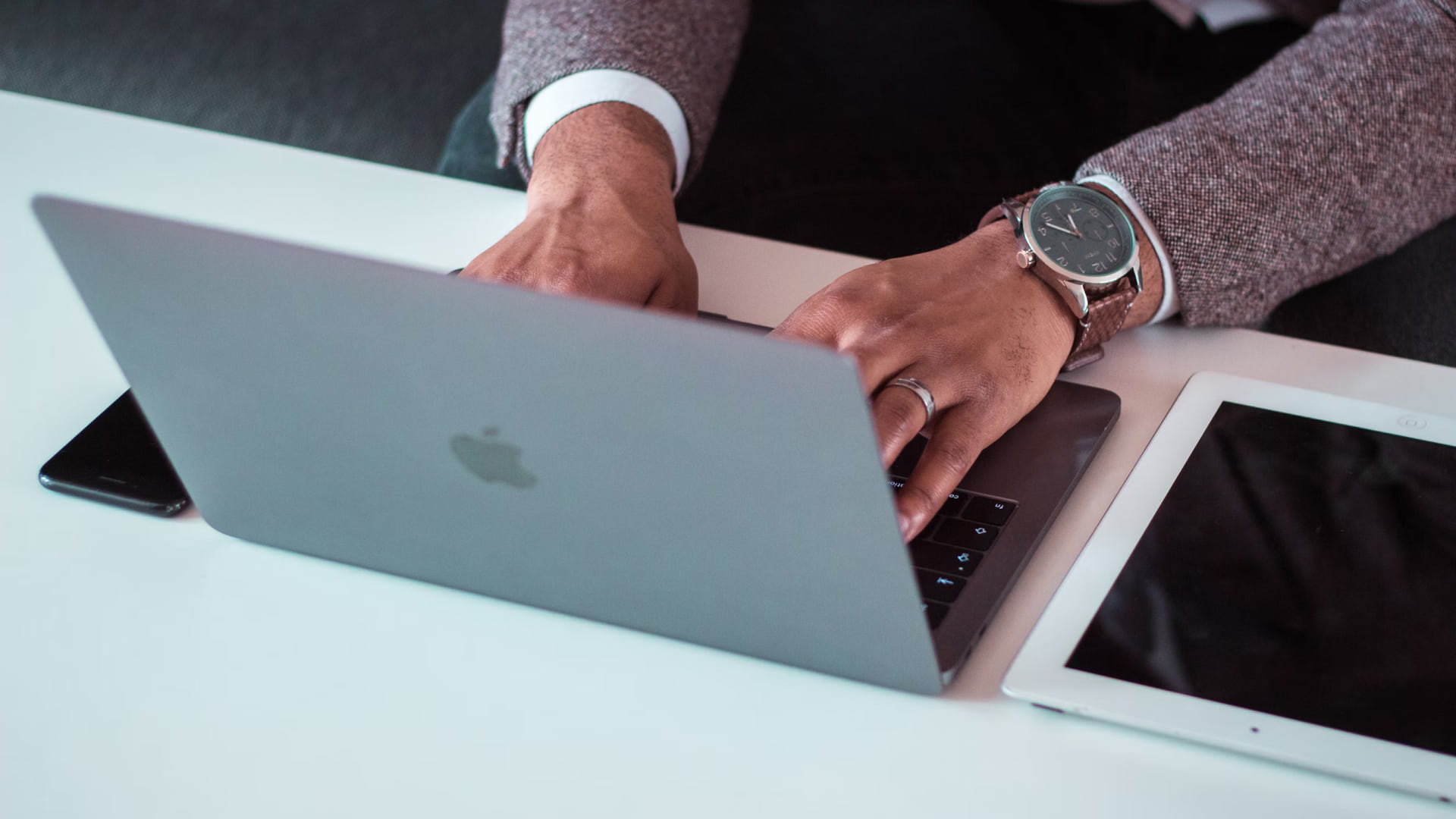 Whissel Strategies A person types on a MacBook laptop at a white desk, with a smartphone and a tablet placed nearby. Toronto Digital Marketing Agency