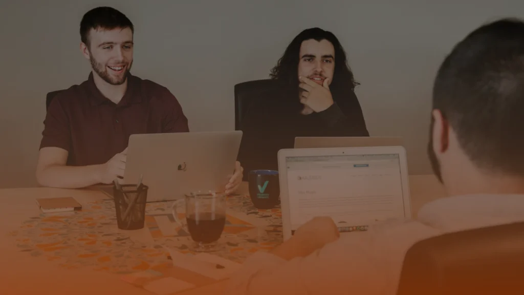 Whissel Strategies Three people sit at a table with laptops, coffee mugs, and documents, engaged in a discussion during a meeting. Toronto Digital Marketing Agency