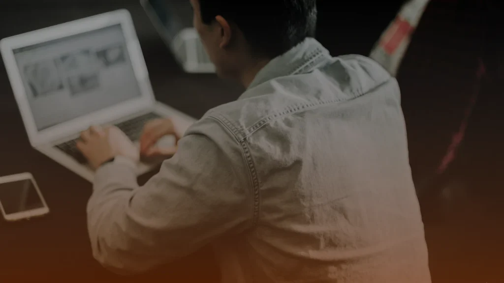 Whissel Strategies Person in a light denim shirt using a laptop at a desk, with a smartphone placed nearby. Toronto Digital Marketing Agency
