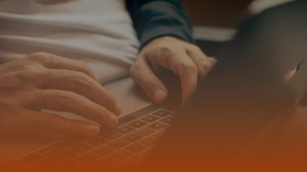 Whissel Strategies Close-up of a person’s hands typing on a laptop keyboard, with an orange gradient overlay at the bottom of the image. Toronto Digital Marketing Agency