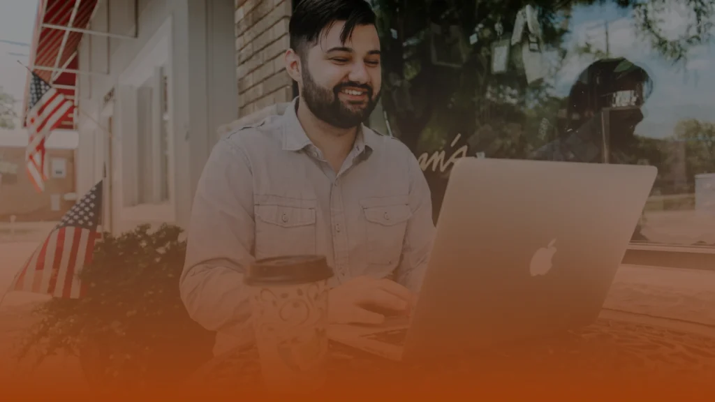 Whissel Strategies A man sits outside at a table with a laptop and a coffee cup, smiling as he works. Toronto Digital Marketing Agency