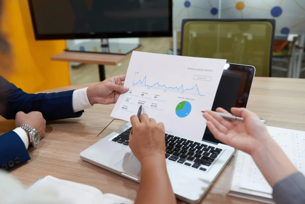 Whissel Strategies Two people review a printed graph and pie chart in front of a laptop during a meeting in an office setting. Toronto Digital Marketing Agency