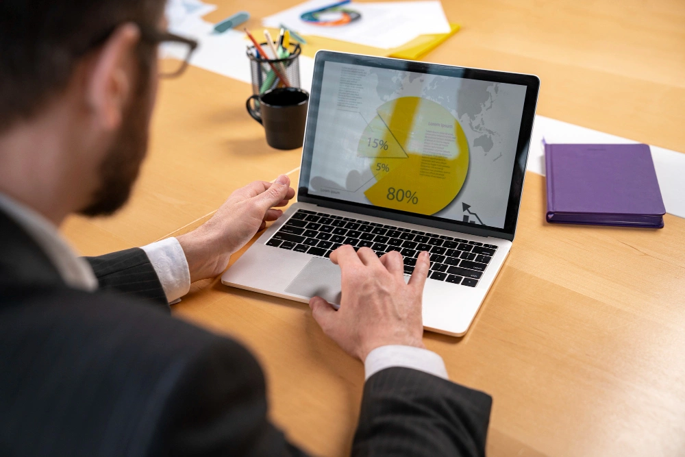 Whissel Strategies A person in business attire works on a laptop displaying a pie chart with yellow segments at a wooden desk with office supplies. Toronto Digital Marketing Agency