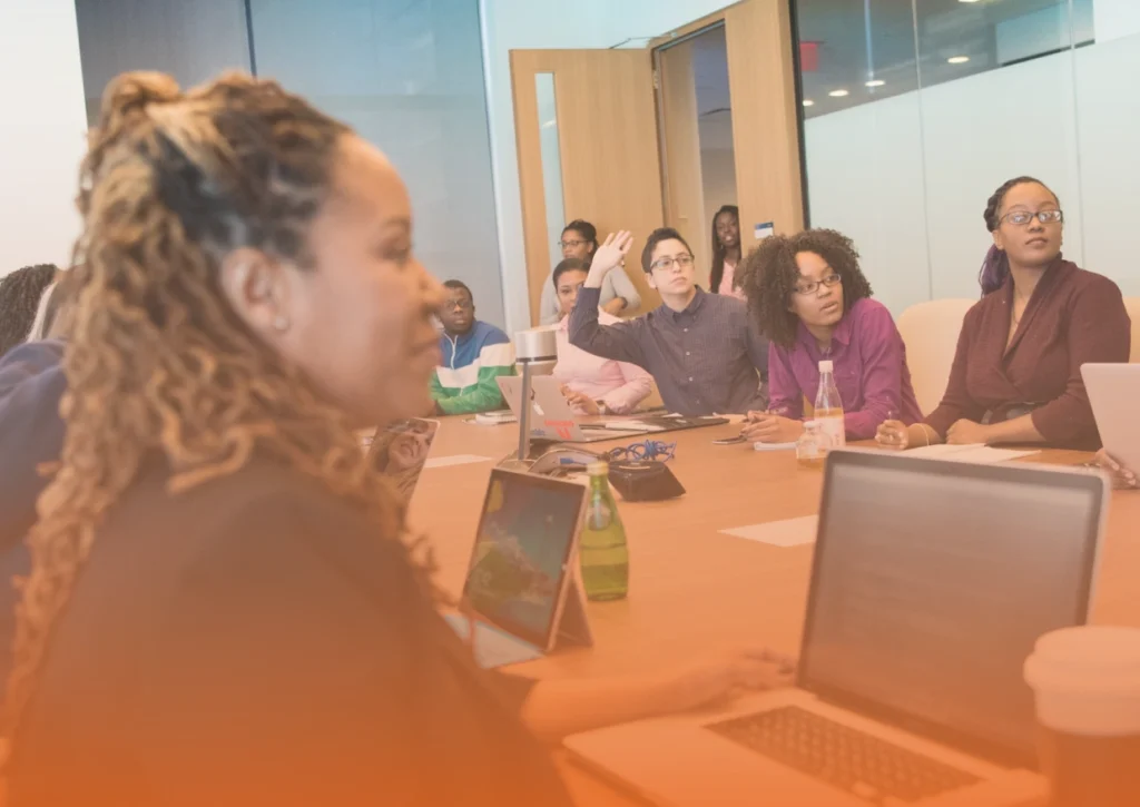 Whissel Strategies A group of people sit around a conference table with laptops and notebooks. One person has their hand raised, and everyone appears to be engaged in discussion. Toronto Digital Marketing Agency